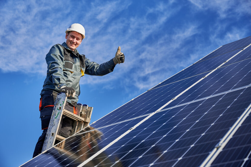 Male worker on solar plant installing solar batteries, standing on a ladder on a sunny day